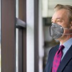 Mature businessman thinking and looking outside the window with mask for protection from corona virus outbreak